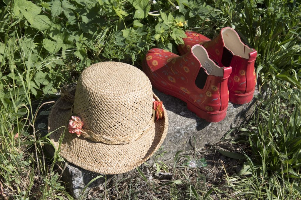 Stiefel und Hut: Ein Wegbegrenzungsstein dient auf diesem Bildnis als Unterlage für rote Kindergummistiefel und einen kleinen geflochtenem Strohhut.